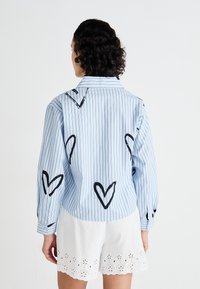 Ljusblå rutig skjorta med svarta hjärtan mönster på ryggen och ärmarna, långa ärmar och knäppta manschetter. Vita ögla kortbyxor.