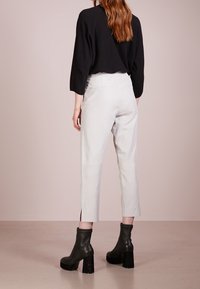 Witte cropped broek met zijsplitten aan de zoom, gecombineerd met een zwarte top en zwarte chunky laarzen met hak. De stof lijkt glad.