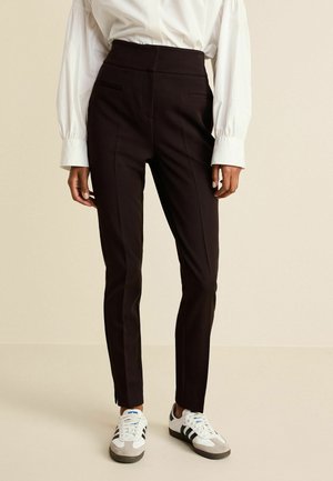 Černé kalhoty na míru s vysokým pasem a bočními kapsami, v kombinaci s bílou košilí a sportovními teniskami. Hladký materiál, slim fit design.