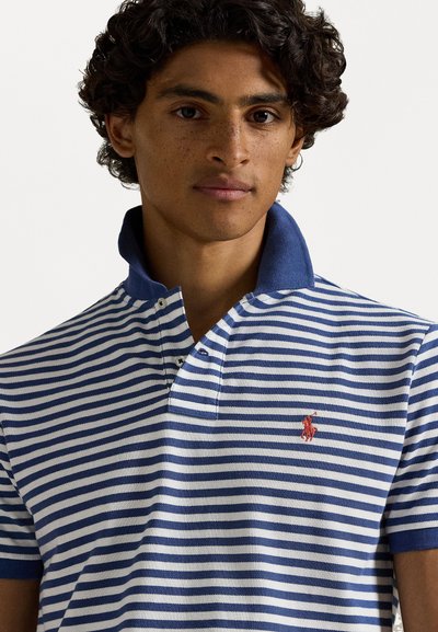 Koszulka polo z naprzemiennymi niebieskimi i białymi paskami, z jednolitym niebieskim kołnierzykiem oraz małym czerwonym logo na lewej piersi. Materiał wydaje się być strukturalny.