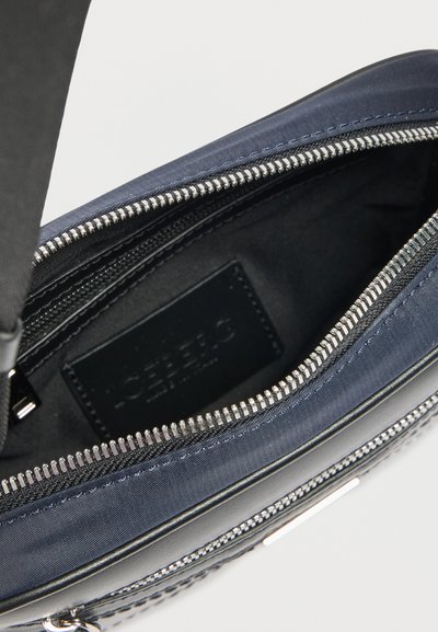 Ανοιχτό μπλε τσαντάκι με φερμουάρ, με ορατή εσωτερική ραφή και μαύρη ετικέτα, που δείχνει ομαλή υφασμάτινη επένδυση και ασημένια δόντια φερμουάρ.