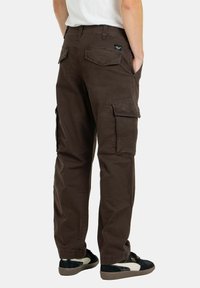 Braune Cargo-Hosen mit entspanntem Schnitt, die mehrere Seitentaschen, gestickte Details und ein Etikett an der Gesäßtasche aufweisen. Der Stoff hat eine matte Textur.