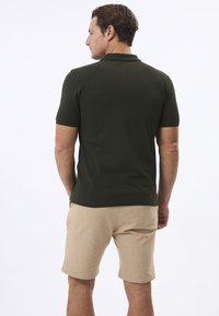 Dunkelgrünes Polohemd mit kurzen Ärmeln, kombiniert mit hellbeigen Shorts. Einfaches Design, glatte Textur und keine sichtbaren Muster oder Akzente.
