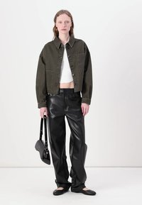 Giacca di jeans verde oliva corta, top bianco a cropped, pantaloni in pelle neri, scarpe basse nere e una piccola borsa nera. Design semplice e strutturato.