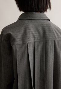 Siva prugasta košulja s klasičnom kragnom, naboranim leđima i krojem prilagođenim figuri, izrađena od teksturirane tkanine sa mekim završetkom.