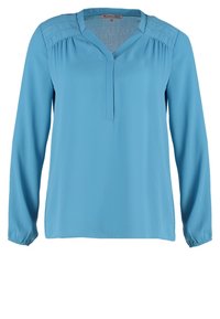 Blouse bleu ciel à manches longues avec col en V, légère fronces aux épaules et surpiqûres décoratives le long des coutures des épaules.