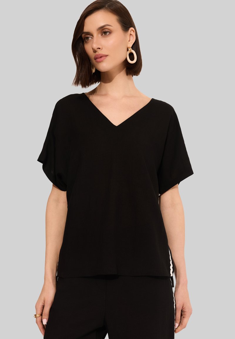 Czarny top z dekoltem w serek i krótkimi, luźnymi rękawami, charakteryzujący się swobodnym krojem i miękkim materiałem. Brak widocznych wzorów lub elementów metalowych.