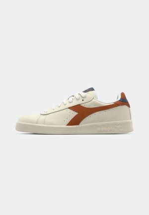 White leather sneaker featuring a brown diagonal stripe, round toe, and textured sole. Blue and red accents on the tongue and heel.