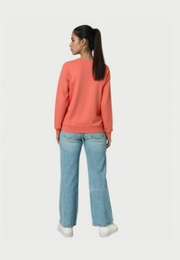 Koronkowa bluza z prążkowanymi mankietami i dołem, połączona z jasnoniebieskimi spodniami o szerokich nogawkach. Modelka stoi tyłem do aparatu, widoczne białe trampki.