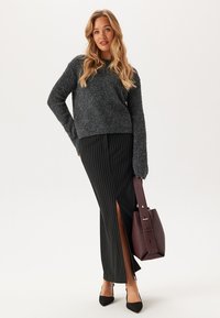 Un pull en laine gris, une jupe maxi rayée noire avec une fente sur le côté, des chaussures noires à bout pointu et un sac à main bordeaux au design structuré.