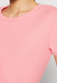 Top corto a maniche corte rosa a coste con scollatura rotonda, caratterizzato da una texture morbida e un design aderente. Sono visibili i dettagli delle cuciture.