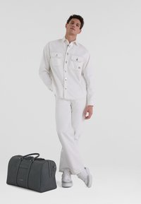 Camisa de mezclilla blanca y pantalones, bolsa de deporte gris con logo, y zapatillas deportivas grises. La camisa cuenta con dos bolsillos en el pecho y botones plateados.