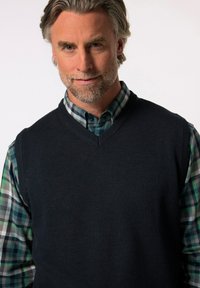 Námořnický pletený svetr s výstřihem do V přes košili s kostkovaným vzorem v zelené a šedé barvě. Důraz na příjemné textury a kontrastní vzory.