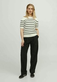Suéter de malha riscado em branco e preto, com mangas curtas. Combinado com calças largas pretas e sapatos escuros.