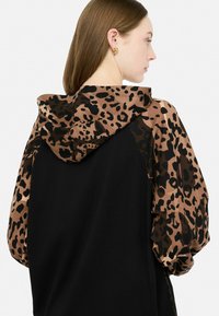Sweat à capuche noir avec un design léopard beige et noir sur la capuche et les manches. Doté d'une coupe décontractée et d'une texture douce.
