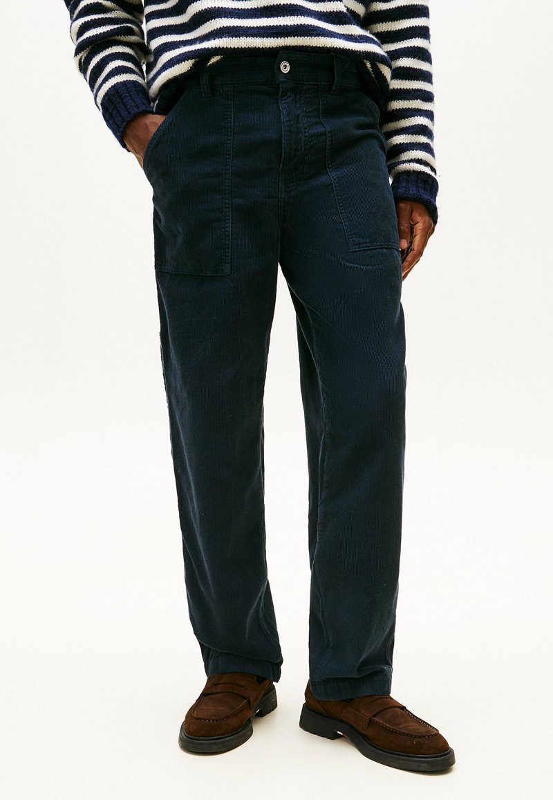Navy corduroy trousers with two front pockets, a straight-leg design, and a textured fabric. Paired with brown loafers.