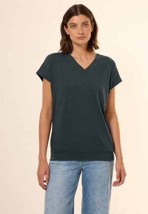 T-shirt grigio scuro a scollatura a V, maniche corte, tessuto morbido, vestibilità rilassata, rifinita con un orlo a costine. Abbinata a jeans wide-leg in denim chiaro.