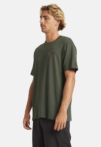 Roheline puuvillane T-särk ümarate kaeluste, lühikeste varrukate ja vasakul rinnal oleva väikese punase logoga. Laudne lõige ja pehme tekstuur.