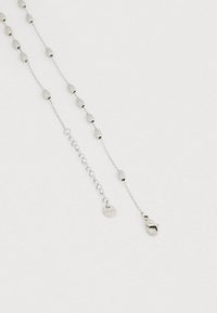 Sudraba ķēdes kaklarota ar ovālas formas pērlītēm, omāra aizdares aizdari un nelielu apaļu uzlīmi ar gravējumu "Liu Jo". Gluda tekstūra un smalka dizaina.