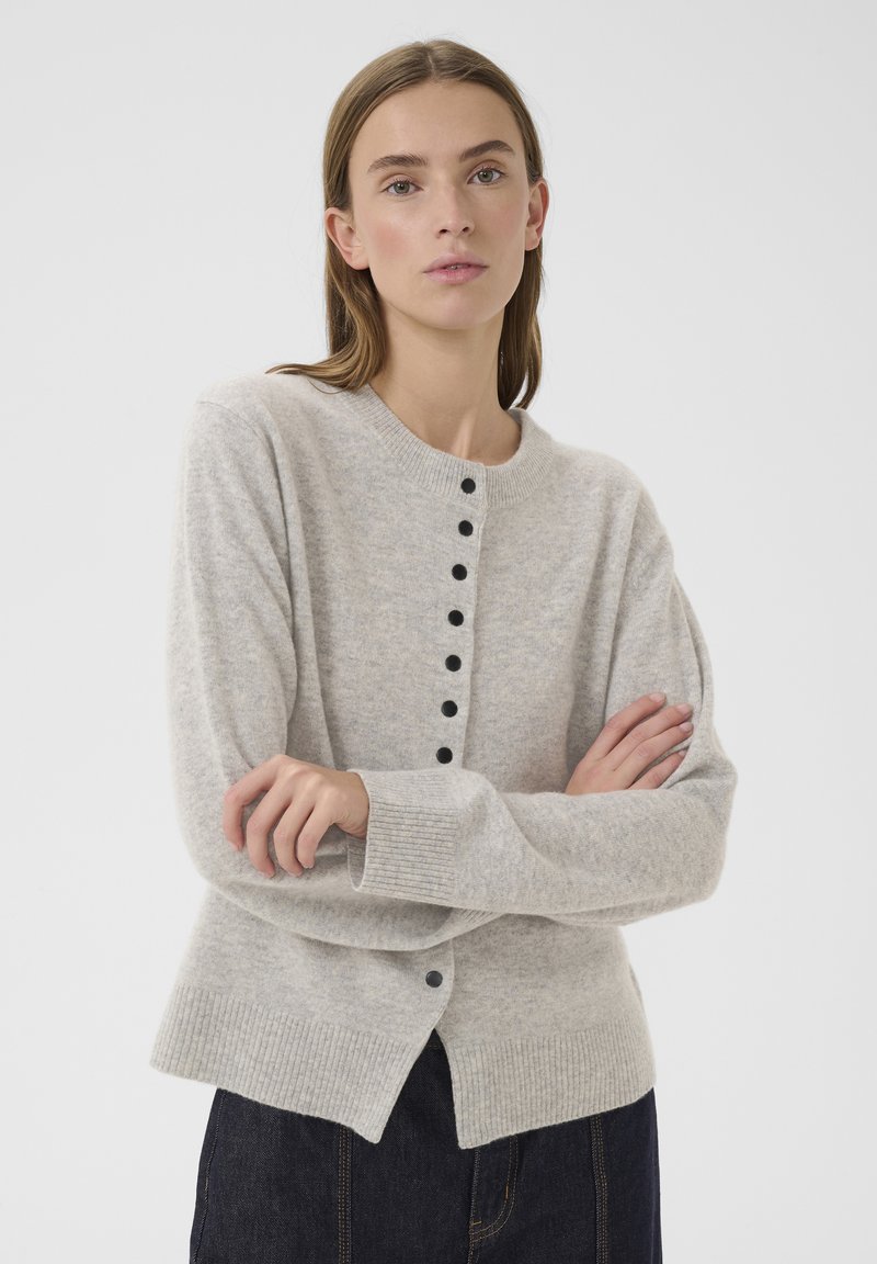 Vaaleanharmaa neuletakki pehmeästä kankaasta, jossa pyöreä kaula-aukko, pitkät hihat ja mustat napit edessä sekä resorireuna.