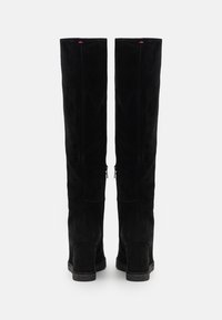 Mustat mokkanahkaiset reiden yli ulottuvat saappaat sileällä tekstuurilla, joissa on kaksi sivuvetoketjua ja hieman korotettu korko. Ylhäällä on punaiset korostukset.