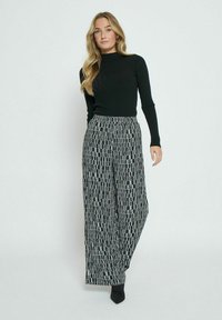 Black long-sleeve top paired with loose-fitting black and white patterned wide-leg pants, featuring an elastic waistband and smooth texture.