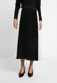 Zwart-witte plisséh-midirok met een brede zwarte tailleband, vervaardigd uit zachte, lichte stof en met een vloeiend silhouet.
