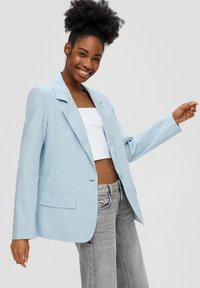 Blazer in lino azzurro con colletto a punta, chiusura a un bottone e due tasche frontali, abbinato a un top bianco corto e jeans grigi.