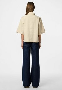 Bežna kratka majica s širokim krojem, uparena s tamnoplavim širokim trapericama, koje ističu glatku teksturu i minimalistički dizajn.