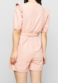 Rosa bomullsoverall med korta puffärmar, volangdetaljer vid axlarna, åtsittande midja och shorts med avslappnad passform.