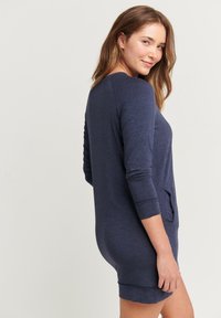 Abito blu navy a maniche lunghe realizzato in tessuto morbido, caratterizzato da una vestibilità comoda e una tasca laterale per la praticità. Texture liscia con cuciture minime.