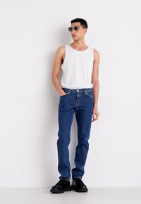 Biela bezrukávová tielko a modré džínsy s uvoľneným strihom. Čierne okrúhle slnečné okuliare a masívne čierne topánky dotvárajú outfit.
