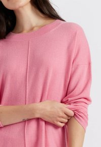 Pull à manches longues en tricot rose doux, avec un col rond côtelé, des coutures d'épaule tombantes et des poignets roulés pour une texture supplémentaire.