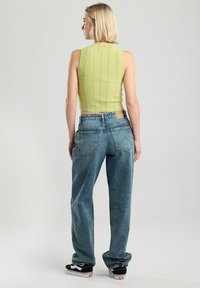 Top corto de canalé verde con cuello alto, combinado con jeans holgados de color azul claro. El conjunto presenta un ajuste relajado y zapatillas negras en contraste.