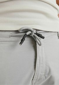 Pantaloni grigio chiaro con chiusura a cordoncino, caratteristiche in plastica nera, cintura piatta e tasche laterali. Tessuto morbido e liscio.