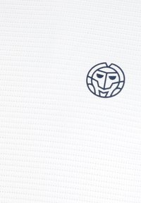 Ein weißer texturierter Stoff zeigt ein kreisförmiges Emblem mit einem stilisierten Gesicht in Marineblau, das sich in der unteren Ecke befindet.