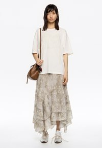Kremowy, oversized t-shirt z teksturowaną grafiką, warstwowa asymetryczna spódnica w stonowanym wężowym wzorze oraz szare sneakersy. Brązowa torba typu crossbody.