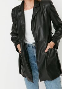 Zwarte leren blazer met een gesneden kraag, sluiting met één knoop en zijzakken, gecombineerd met lichtblauwe denim jeans.