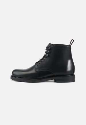 Botas de cuero negro hasta el tobillo con punta redondeada, diseño con cordones, superficie texturizada y un tacón plano y robusto para mayor estabilidad.