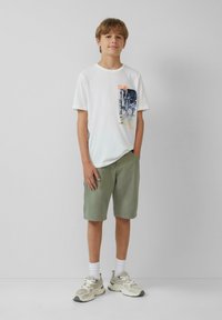 Witte katoenen t-shirt met grafische print, lichtgroene shorts en grijze sneakers. Korte mouwen en relaxed fit. Draag het met witte crew sokken.