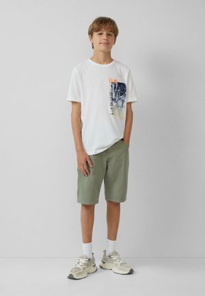 Witte katoenen t-shirt met grafische print, lichtgroene shorts en grijze sneakers. Korte mouwen en relaxed fit. Draag het met witte crew sokken.