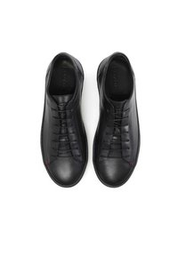 Zapatillas de cuero negro con una textura suave, diseño de cordones, puntera redondeada y sutil acento rojo cerca de los cordones. Presenta una suela plana de goma.