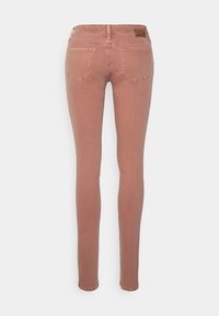 Jeans ajustados de color rosa con una textura suave, diseño de cinco bolsillos y cierre de botón. Incluye detalles de costura y una etiqueta de la marca.