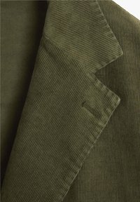 Chaqueta de pana verde oliva con revers, que presenta una textura acanalada distintiva y detalles ajustados en el cuello y los bordes.