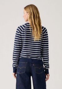 Suéter a rayas en azul marino y blanco con dobladillo acanalado, mangas largas y un ajuste holgado, combinado con jeans de mezclilla oscura.