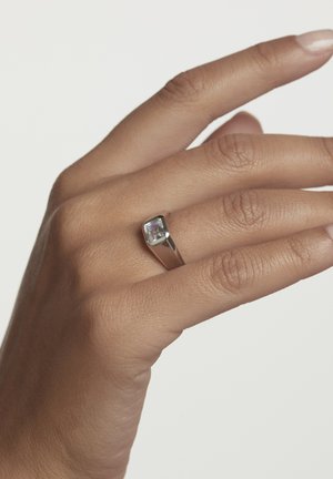 Silberring mit einem quadratischen, klaren Stein, der in einem polierten Band gefasst ist; getragen an einer Hand mit glatter Haut und natürlich lackierten Nägeln.