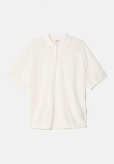 Polo-shirt blanc à manches courtes en tricot texturé avec un col classique et une patte de boutonnage à trois boutons. Présente une coupe décontractée et oversize.