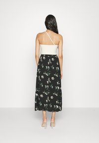 Robe maxi avec un haut crème, une bretelle. Jupe noire arborant un motif floral en rose et vert. Tissu lisse, design fluide.