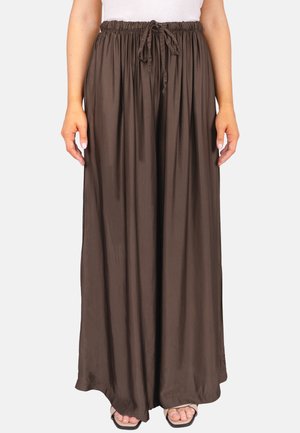 Femme portant un pantalon ample couleur brun foncé avec une taille élastique et un cordon, associé à un haut blanc et des sandales ouvertes.