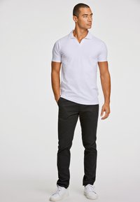 Valkoinen lyhythihainen poolopaita, jossa pehmeä tekstuuri, yhdistettynä mustiin housuihin ja valkoisiin tennareihin, mikä luo yksinkertaisen, rentoa ilmeen.